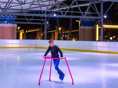 Niño aprendiendo a patinar en pista de hielo climatizada con soporte por la noche.