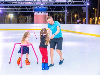 Dos niñas aprenden a patinar sobre hielo con un hombre por la noche en una pista de hielo.