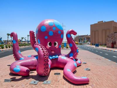 Aufblasbarer pinker Oktopus mit blauen Punkten auf einem Bürgersteig bei klarem Himmel.