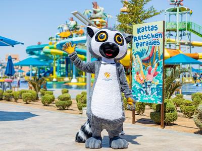 Person im Lemurenkostüm im Freizeitpark vor bunten Wasserrutschen und Pflanzen.