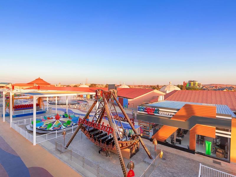Outdoor-Freizeitpark mit Schaukeln, Karussells und roten Dächern unter klarem blauem Himmel.
