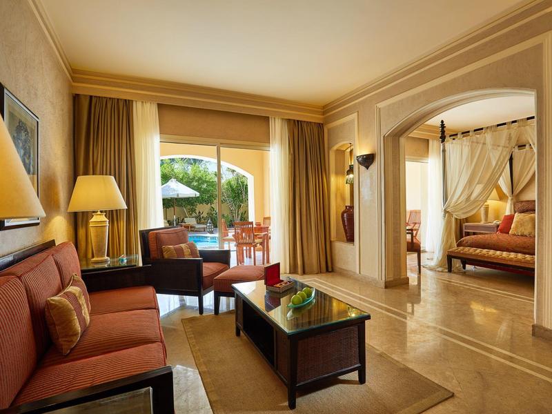 Suite de hotel luminosa con sala de estar y vista a terraza con área de jardín.