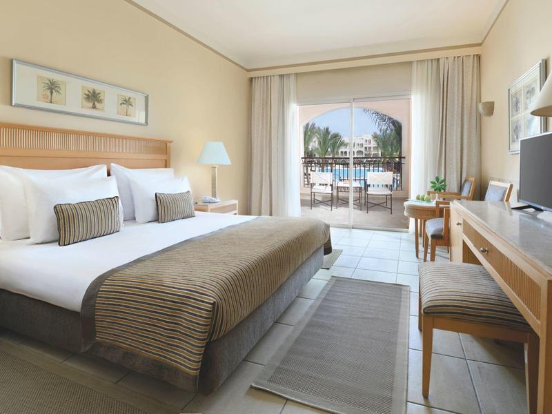 Habitación de hotel con cama doble, escritorio, TV y balcón con vistas al exterior.