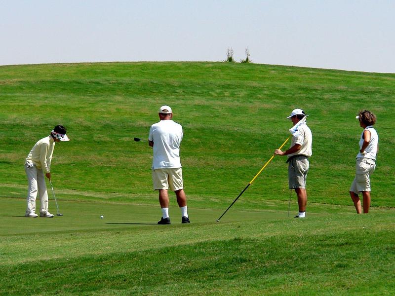 Cuatro personas juegan golf en un campo verde bajo un cielo despejado.