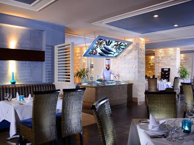 Moderne restaurantinterieur met gedekte tafels, stijlvolle stoelen, sfeerverlichting en een digitaal scherm.