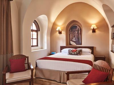 Camera accogliente con finestre ad arco, letto matrimoniale, poltrone e illuminazione calda.