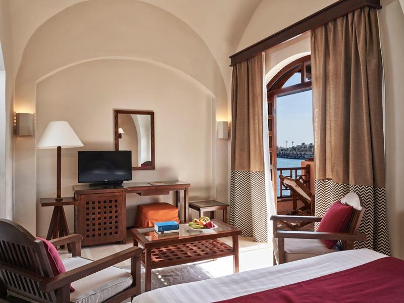 Camera d'hotel accogliente con arredamento rustico, balcone con vista mare e mobili in legno.