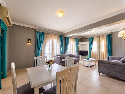 Ampio soggiorno d'hotel con tende blu, divani grigi, tavolo da pranzo e grandi finestre.