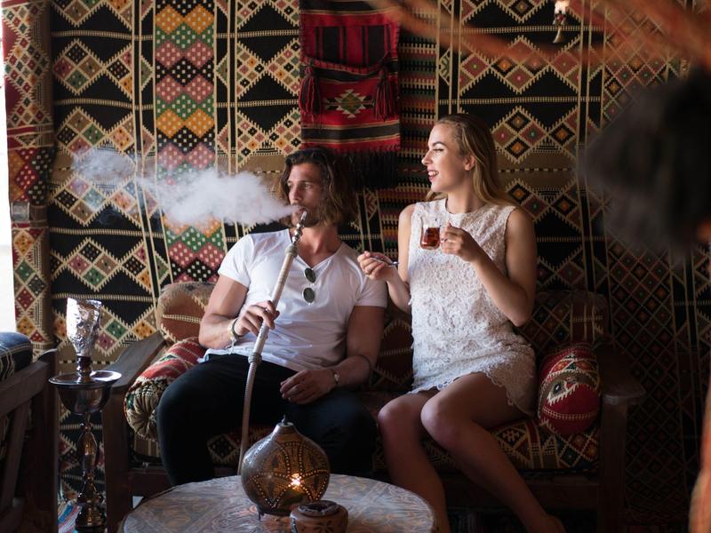 Coppia seduta in stanza decorata, donna con bicchiere di tè, uomo che fuma narghilè