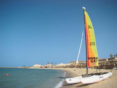 A sailboat on the beach with clear blue sky and buildings in the background.