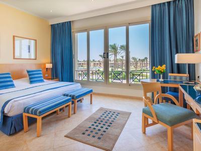 Lichte hotelkamer met groot bed, blauwe accenten en uitzicht op een buitenzwembad.