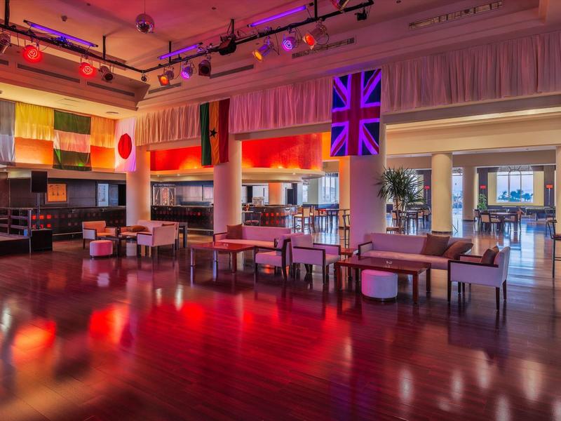 Moderne hotel lounge met kleurrijke vlaggen, stijlvolle zitgedeeltes en warm licht.