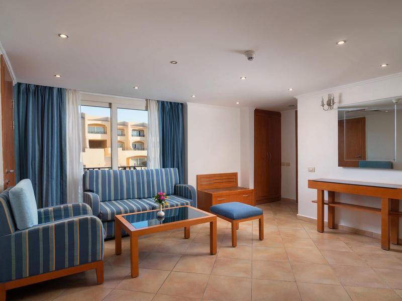 Lichte hotel-lounge met blauwe stoelen, bank, houten tafel en grote spiegel aan de muur.