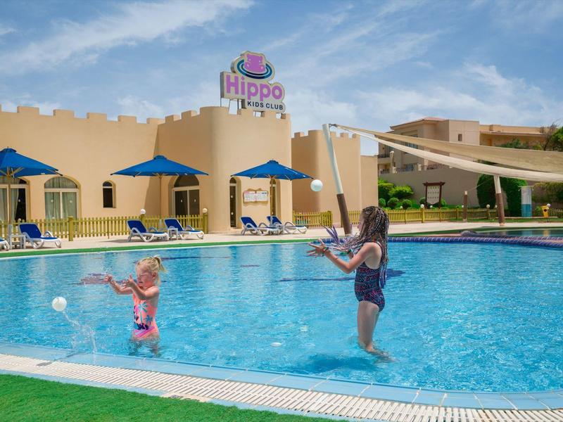 Kinderen spelen met netten bij het blauwe zwembad voor Hippo Hotel op een zonnige dag.