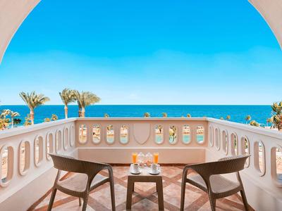 Terrazza con due sedie e un tavolo con vista su palme e mare in una giornata di sole.