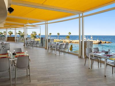 Open restaurant met gele zonwering en uitzicht op zee en palmbomen.