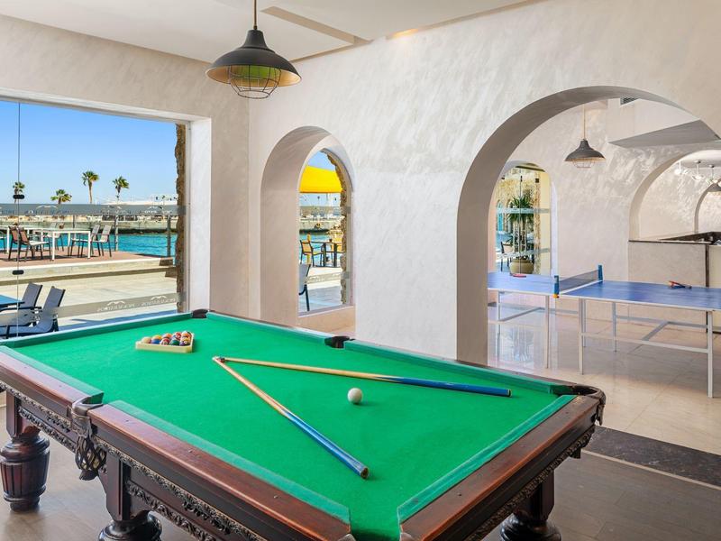 Tavolo da biliardo e tavolo da ping pong in una stanza giochi luminosa e aperta con vista sul mare.