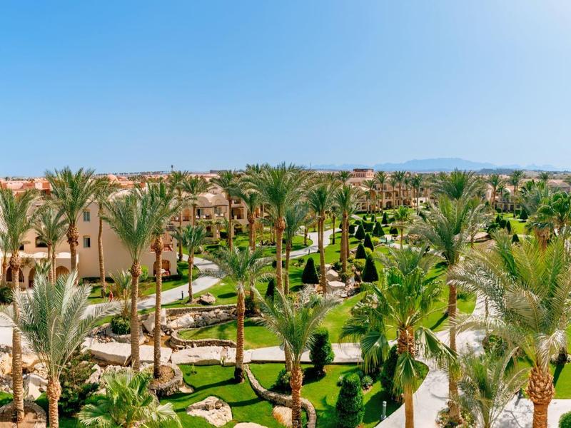 Vista panoramica di un resort con piscine, palme e edifici color sabbia sotto un cielo limpido.