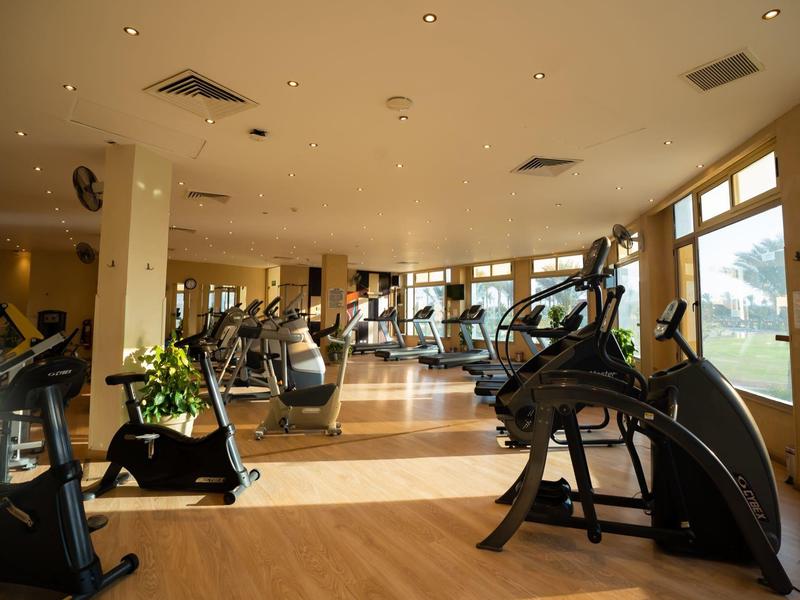 Lichte fitnessruimte met grote ramen en diverse trainingsapparaten.