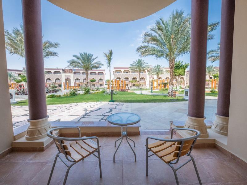 Uitzicht vanaf een overdekt terras op een tuin met zwembad en palmbomen bij een hotel.