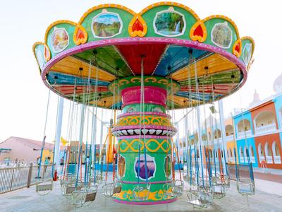 Colorfully painted carousel with empty swing seats in an amusement park during daylight.