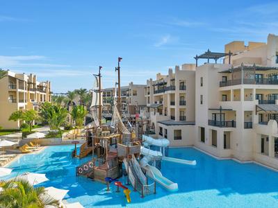 Hôtel avec grand piscine, toboggans aquatiques et aire de jeu en forme de bateau pirate sous un ciel dégagé.