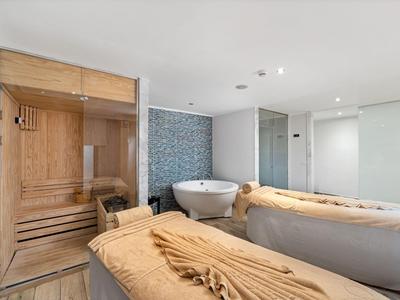 Salle de bien-être moderne avec sauna, table de massage et baignoire dans une ambiance calme.