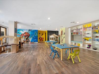 Grande salle de jeux pour enfants lumineuse avec des tables colorées, des chaises et des étagères pleines de jouets.