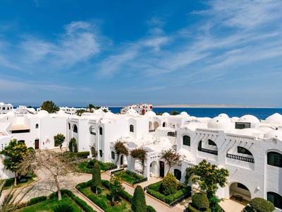 Weißes Hotel im mediterranen Stil mit grünen Gärten und Blick auf das blaue Meer unter blauem Himmel.