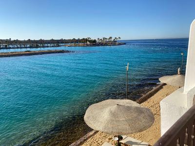 Klares blaues Meer, Strand mit Sonnenschirm und Küstenlinie bei klarem Himmel.