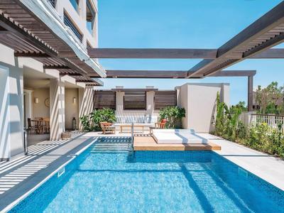 Piscina azzurra con lettini e pergolato moderno sotto un cielo limpido.