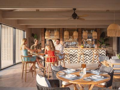 Helle Hotelbar mit Gästen, die Getränke genießen, umgeben von Stühlen, Tischen und natürlicher Beleuchtung.