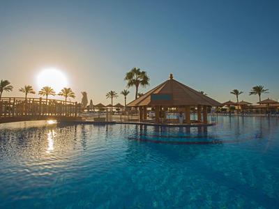 Gran piscina al aire libre con sombrillas y palmeras al atardecer en un resort.