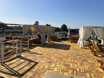 Ampia terrazza solarium con pavimento in legno, aree coperte e sdraio sotto un cielo limpido