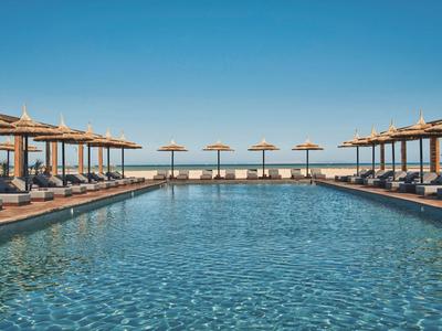 Grande piscina con lettini e ombrelloni sotto un cielo azzurro limpido.