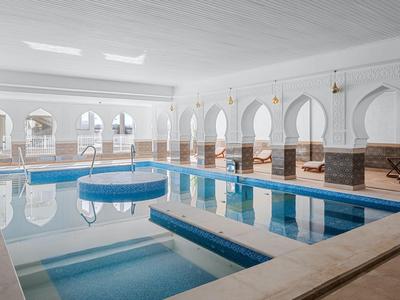 Elegancki kryty basen z niebieskimi basenami, architektonicznymi łukami i miejscami do siedzenia w hotelu.