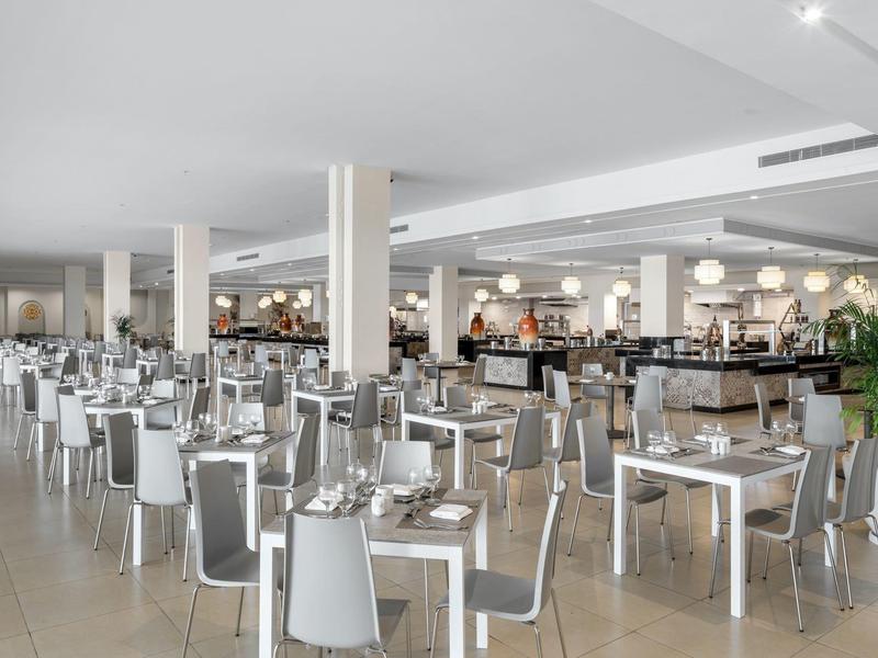 Ampia sala da pranzo moderna con tavoli bianchi e sedie grigie.