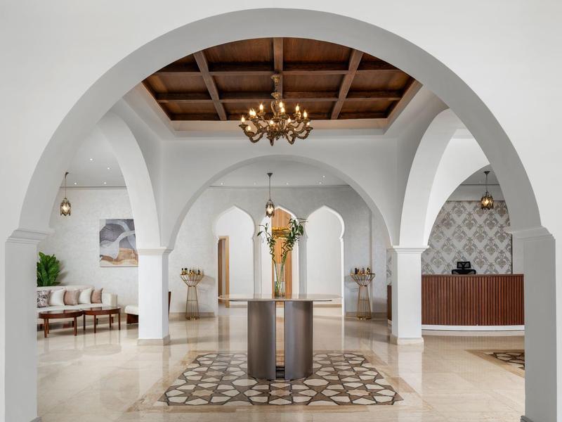 Ampia hall di hotel luminosa con archi, lampadario e decorazione centrale su tappeto