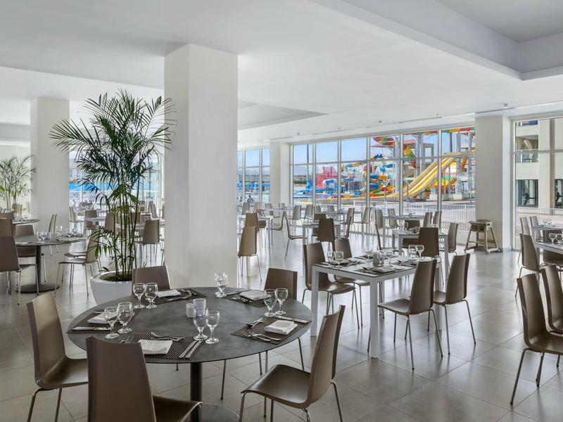 Sala da pranzo luminosa arredata con tavoli rotondi e sedie, vista su un'area piscina