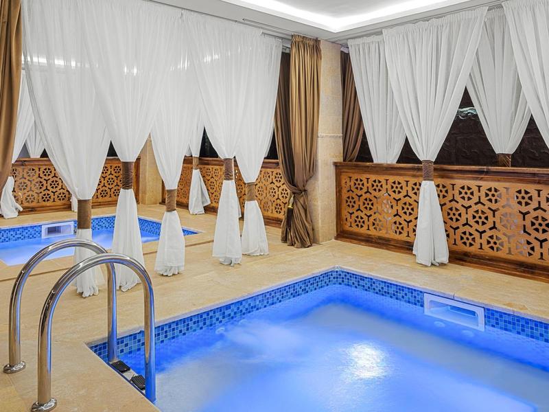 Piscina interna con illuminazione blu circondata da tende e pannelli murali decorativi.