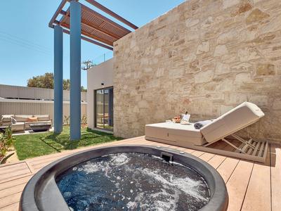 Outdoor hot tub on wooden deck beside comfortable lounge chair and stone wall under blue sky