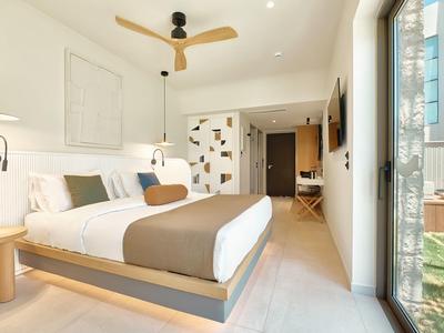 Modern hotel room with double bed, ceiling fan, and balcony access overlooking outdoors.