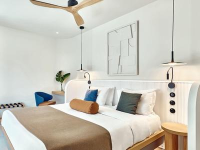 Modern hotel room with double bed, brown throw, artwork, and two hanging lamps.