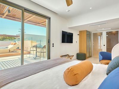 Modern hotel room with bed, terrace, and sea view in sunny weather.