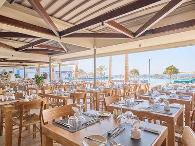 Großes, offenes Restaurant mit Holztischen und Blick auf das Meer bei Sonnenschein.