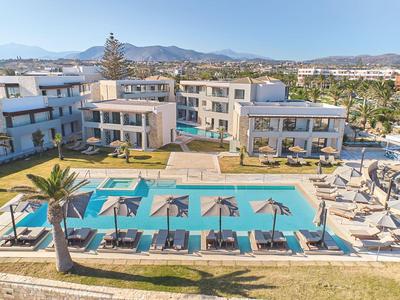 Moderner Hotelkomplex mit großem Pool, Sonnenliegen und Sonnenschirmen im Freien unter blauem Himmel.