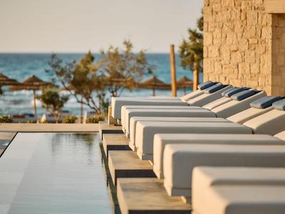 Reihen von Liegestühlen am Pool mit Blick auf das Meer und Sonnenschirme.