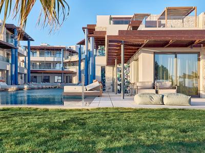 Moderner Hotelkomplex mit Pool, Liegen und grüner Wiese unter klarem Himmel