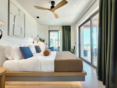 Modern hotel room with large bed, ceiling fan, and floor-to-ceiling windows overlooking balcony.