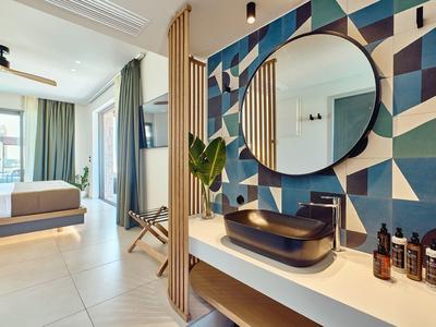 Modern hotel room with open bathroom, geometric wall design, and large windows.